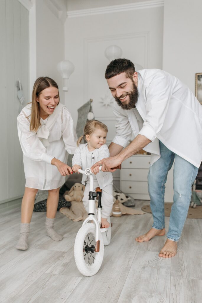 pexels-photo-7220969-7220969 Freudige familiäre Bindung drinnen, während Eltern dem Kind auf dem Fahrrad helfen. Heller und fröhlicher Moment.